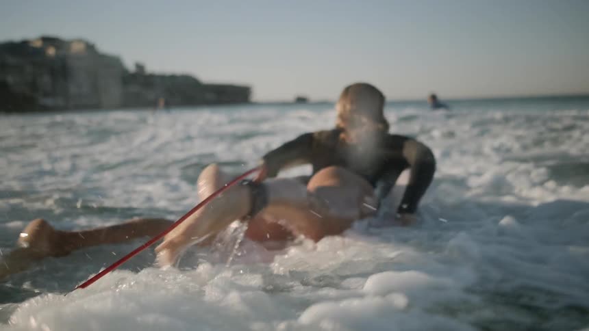 The woman jumps on her surfboard in the water