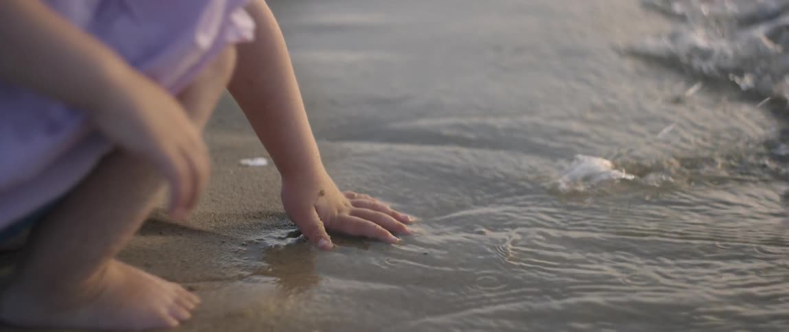 A girl presses her hand into the wet sand leaving a print