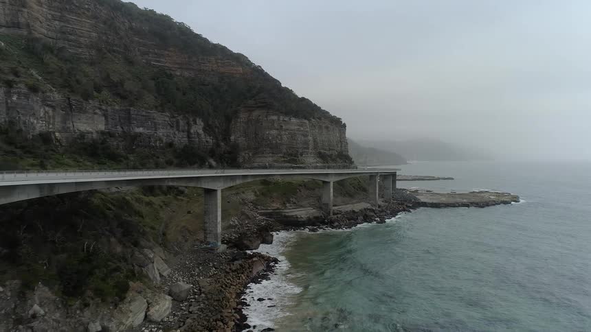 A car travels on a coastal road on a foggy day