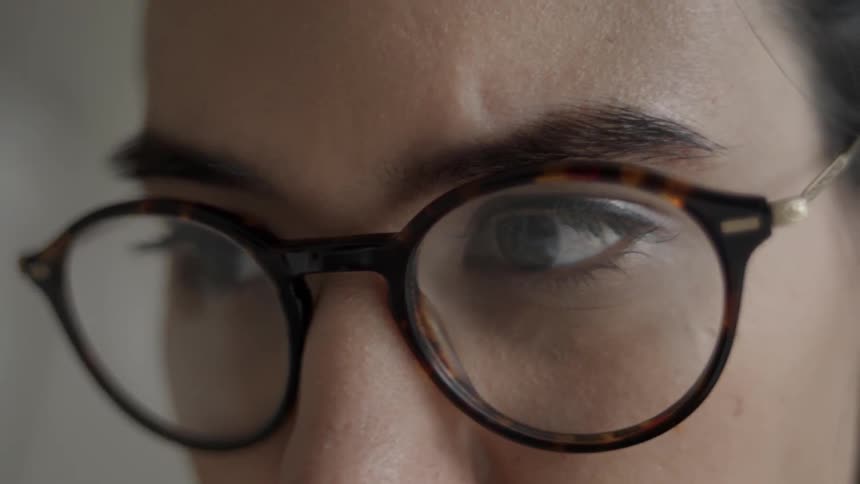 A woman wearing glasses is reading while she sits working inside in daylight