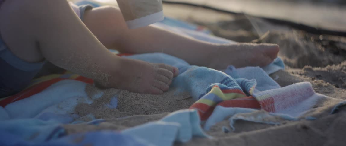 A toddler plays in sand on a beach