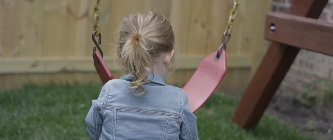 A little girl is playing with a swing seat outside in a backyard in daylight