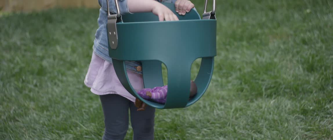 A toddler girl plays with a doll in a swing outside