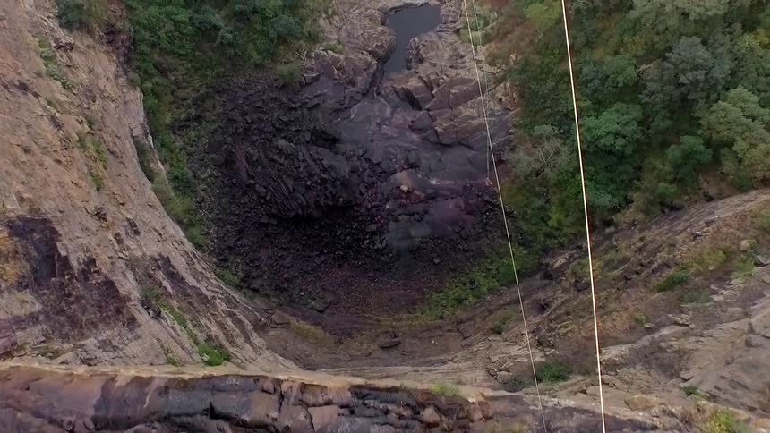 View from above a large steep cliff with people riding a zip line underneath