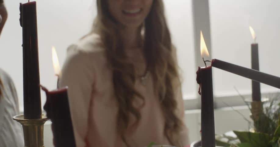 A woman sitting at a dinner table and someone lighting candles