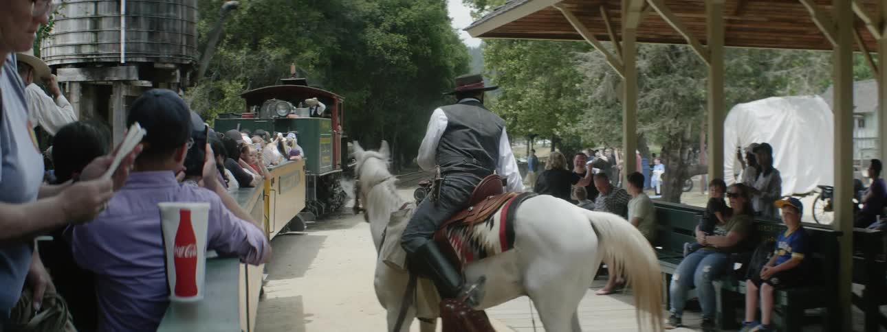 A man on a horse talks to tourists sitting on train cars