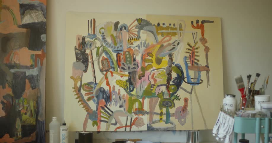 A colorful painting is sitting on an easel inside an artist's studio in daylight