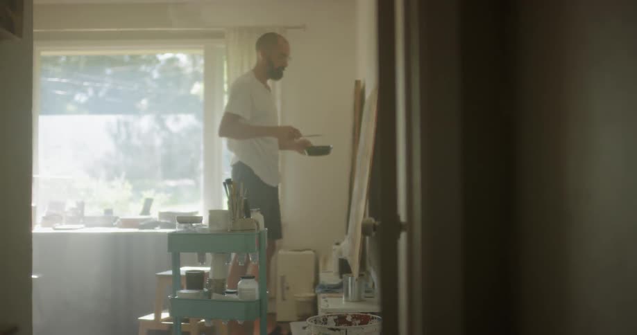 An artist is painting on a large canvas inside in daylight
