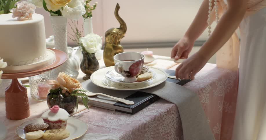 A woman setting a large spoon next to a saucer and plate on a table that is adorned with flowers, cakes and pastries