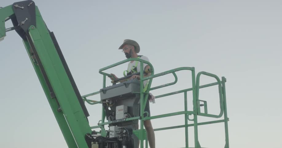 Man stands in a caged area at the top of a piece of machinery