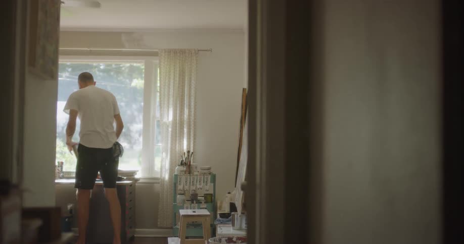 An artist is placing a step stool in front of a canvas inside his studio in daylight