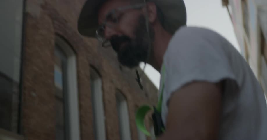 Man wearing glasses and a hat stands between the tall buildings