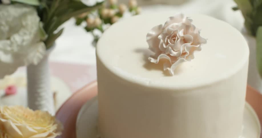A white wedding cake with a flower on top next to a vase full of flowers