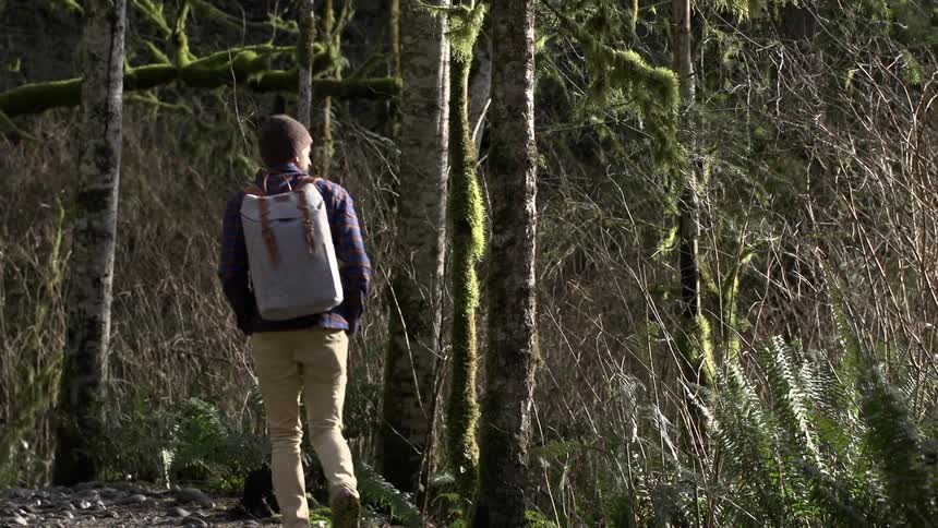 A man in a knit cap hikes a dirt path in a wooded area