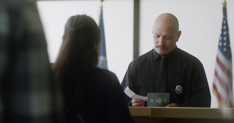 A man checks a woman's passport in front of an american flag