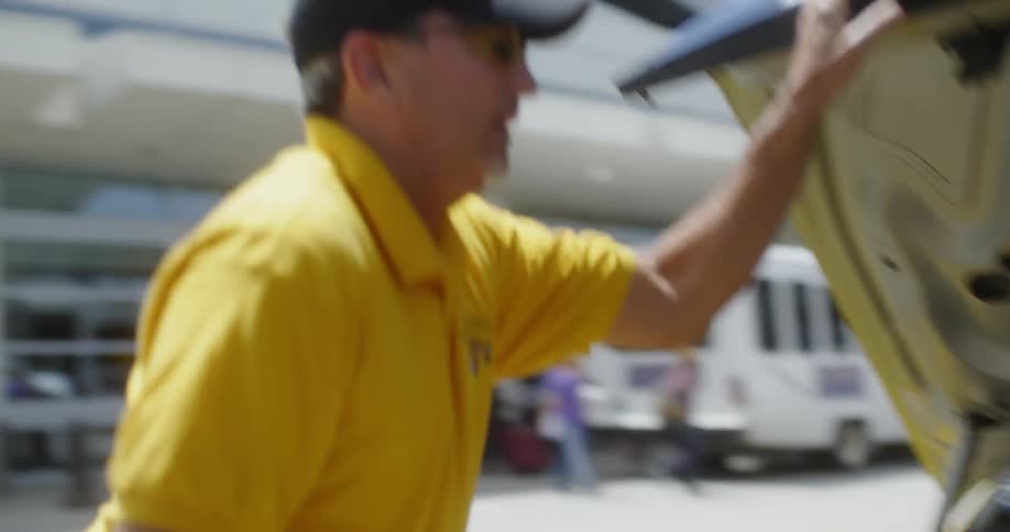 A taxi driver loads a suitcase into a yellow taxicab