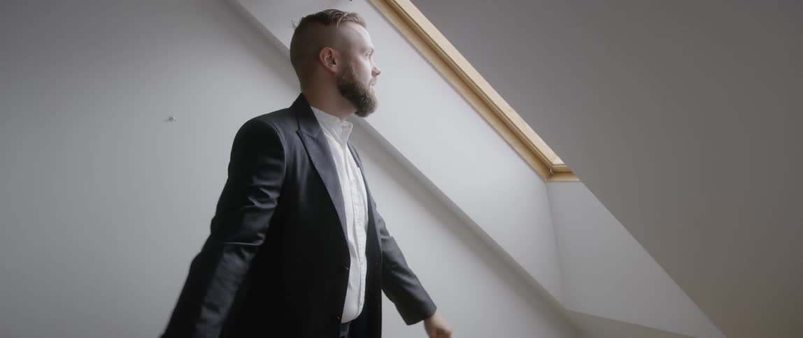 The man adjusts his jacket near the window