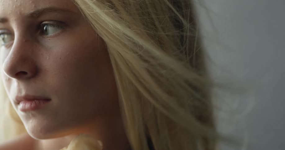 A blonde woman holding yellow flowers and gazing at something while a breeze blows her hair