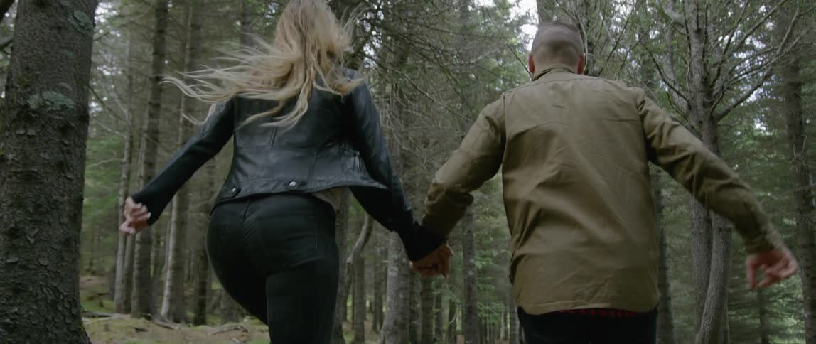 A man and woman hold hands while running in a forest