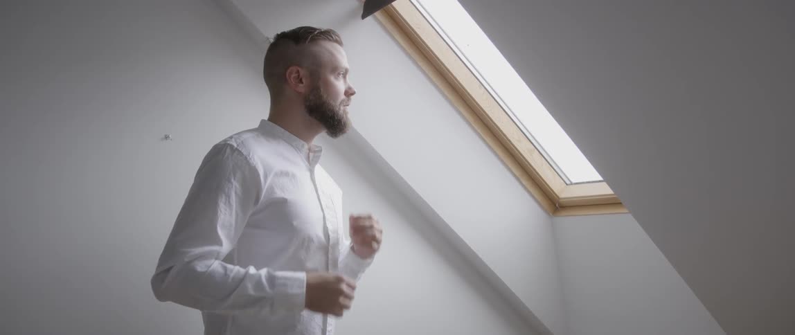 The man adjusts his clothes by the window
