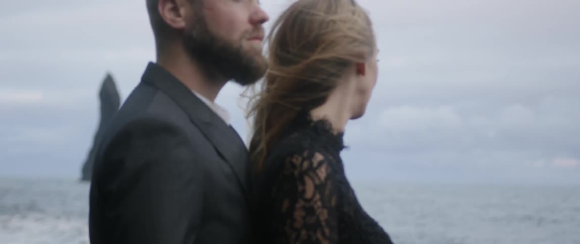 A man and woman stand on a beach on a cloudy day