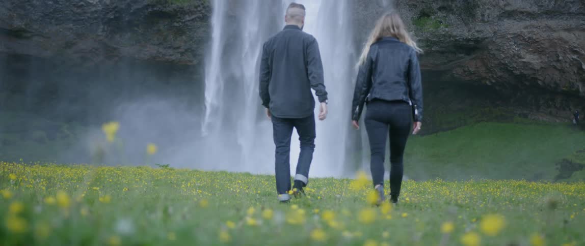 A man and woman walk towards a waterfall