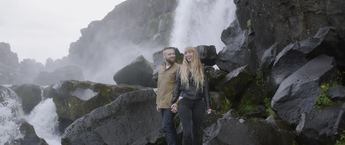 The couple hold hands by the waterfall