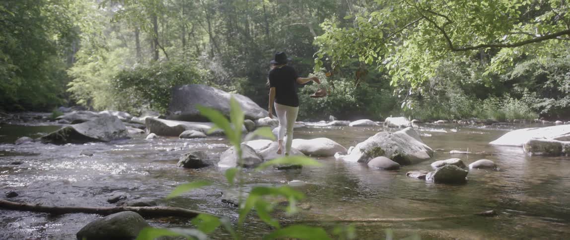 A woman balances on rocks while crossing a stream