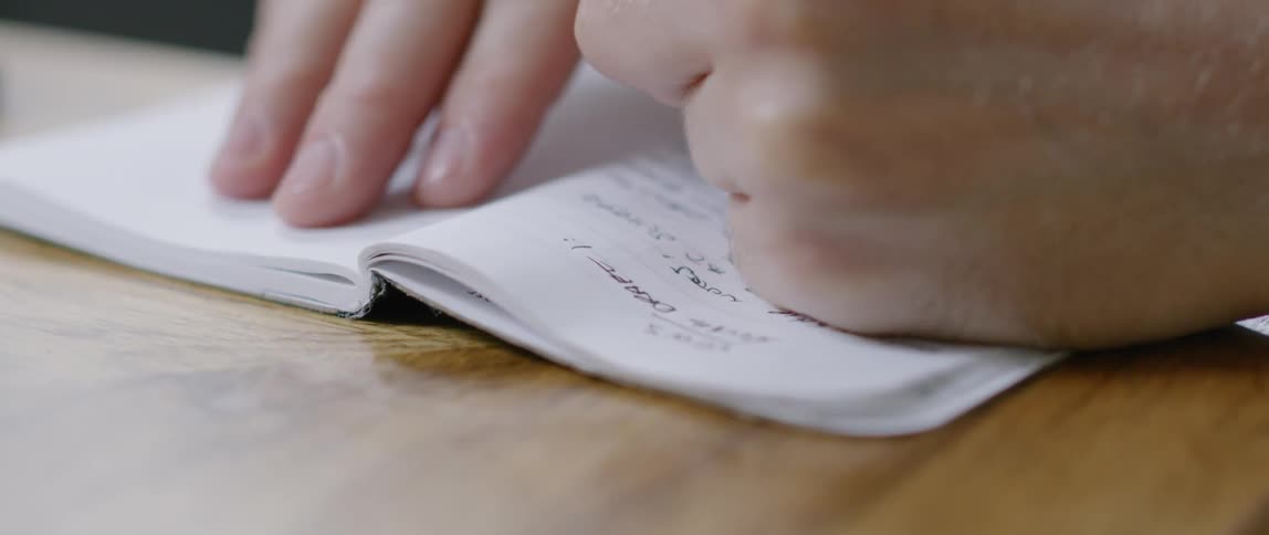 A person writes in a small notebook