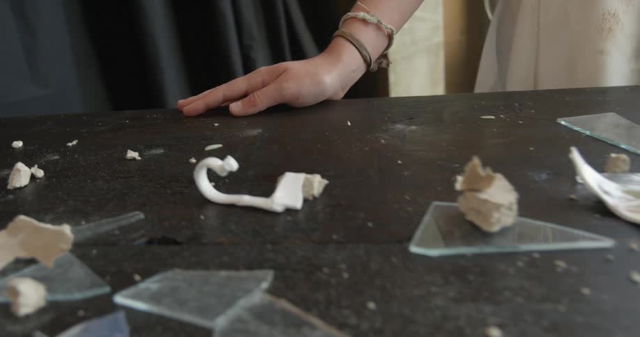 A woman runs her hand along a table covered with broken glass