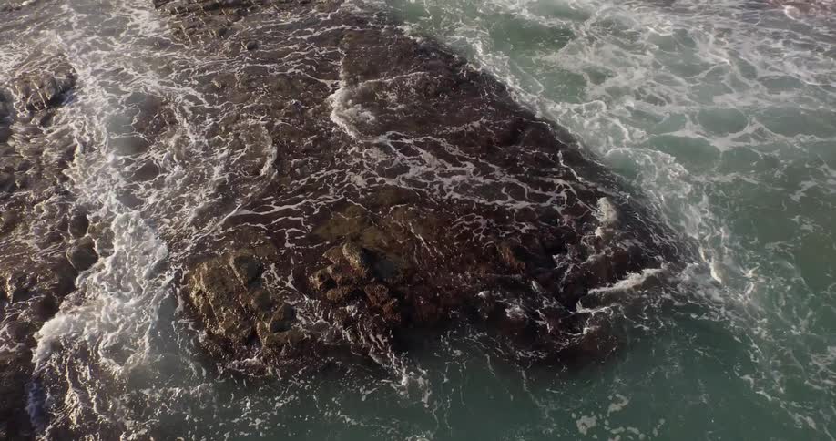 Aerial view of rough waters on the coat going over large rocks