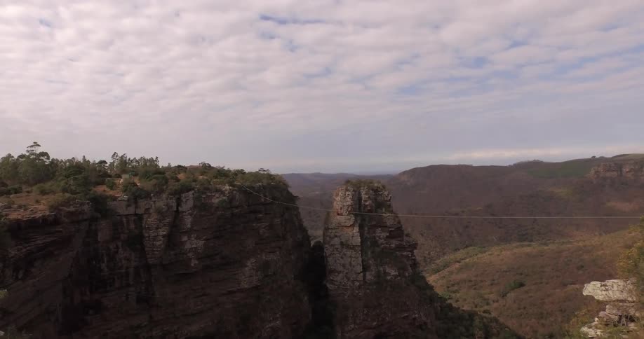 View of people walking over a very small bridge going over two tall mountains