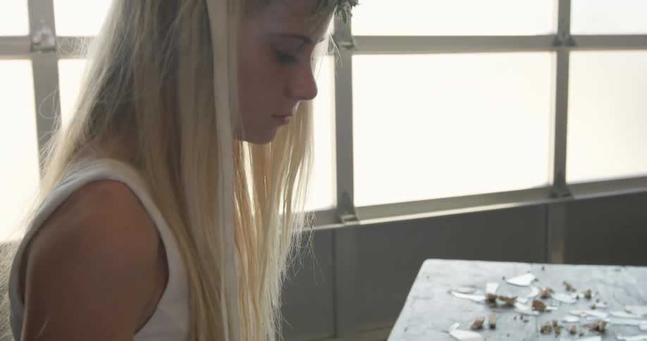 A blonde woman is standing at a table of broken glass