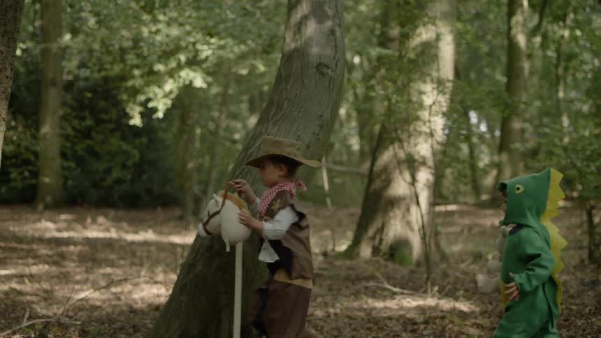 Several children wearing costumes run through the woods on a sunny day