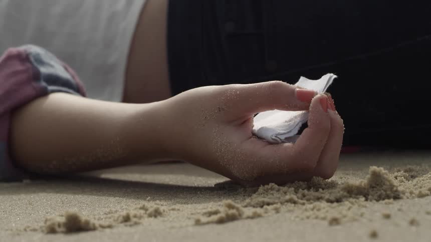 The person holds a note in their hand on the sand