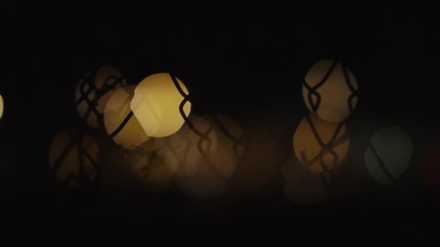 The lights shine behind the fence at night