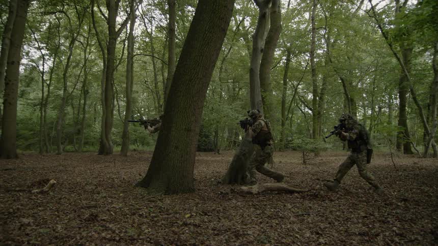 Military members run through a forest with their guns drawn