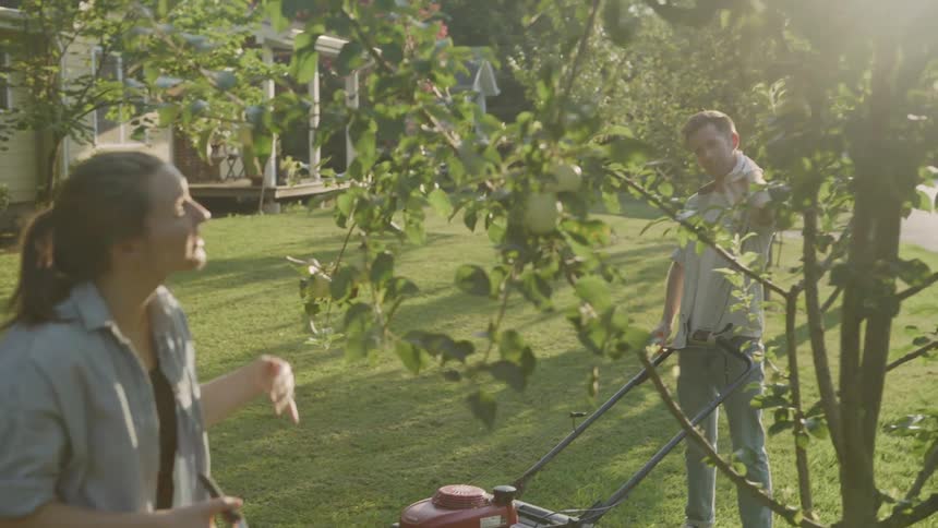 The woman trims a tree as a man wipes his face with a rag