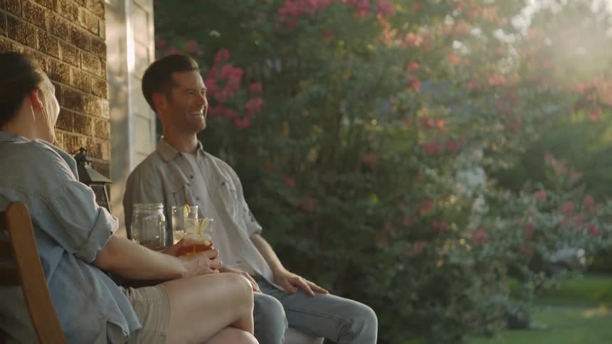 Man and woman sit on a porch smiling and drinking
