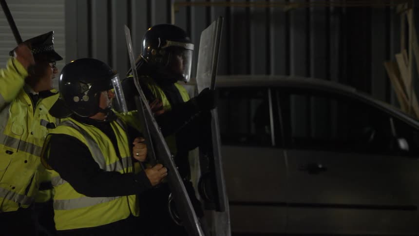 Security guards yell and wave their batons while holding large fields