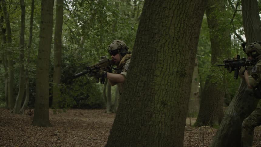 Soldiers shoot guns while running through the woods