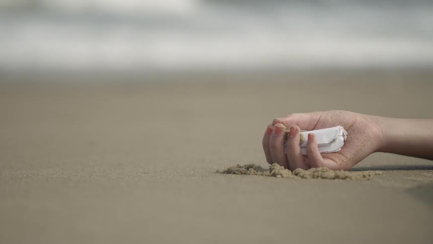 The person is lying in the sand holding a note