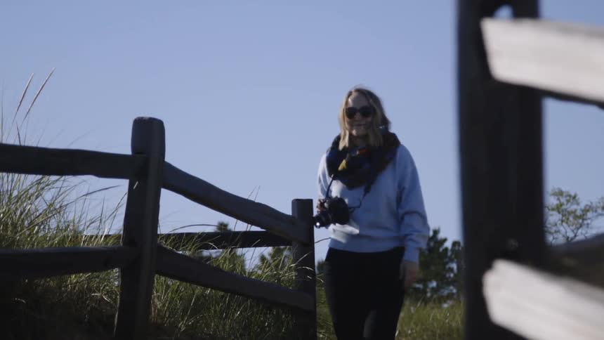 The woman is carrying her camera on a sunny day