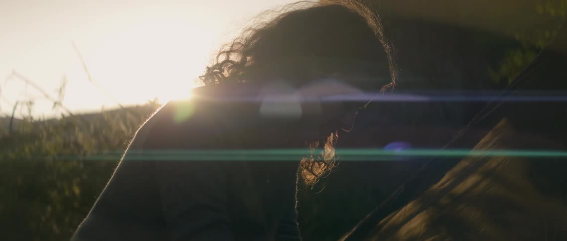 The woman is leaning forward in the yard at sunset