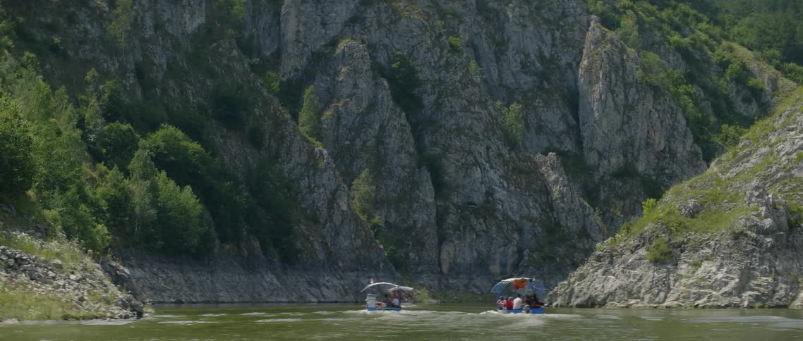 Many people rides on two boats on a river next to tall mountains