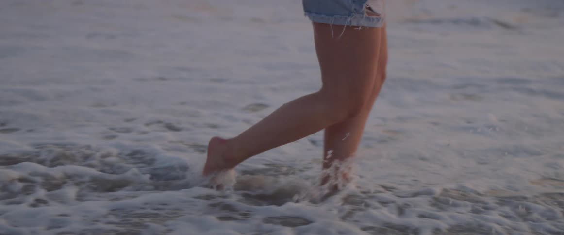 Woman is smiling while wading in ocean water at sunset