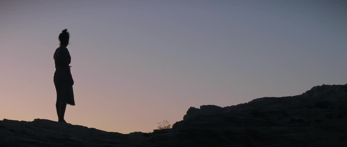Woman stands outside on hilly landscape at sunset