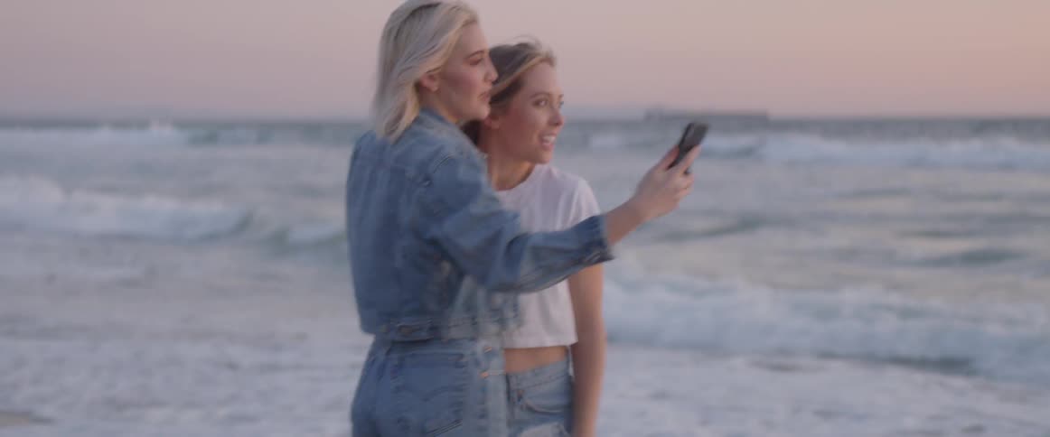 Two women hug and take a photo on the beach