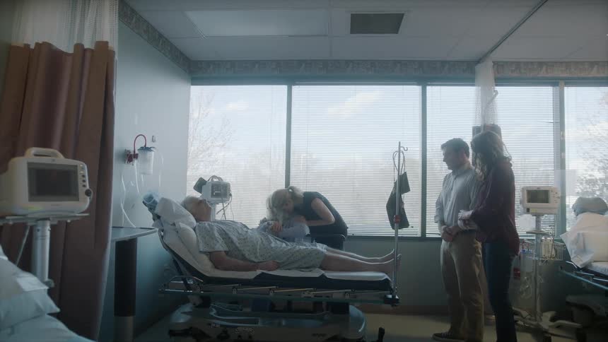 Several people surround a man lying in a hospital bed