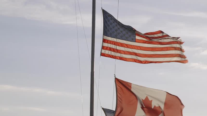 An American and Canadian flag blow in the breeze as they hang on a flagpole